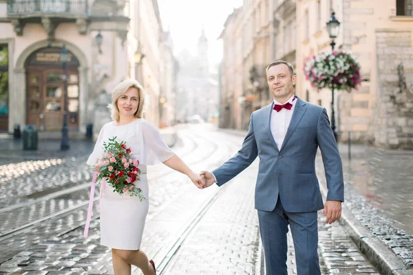 Portrét šťastného páru středního věku v lásce, držící se za ruce, mající rande ve starobylém městě — Stock fotografie