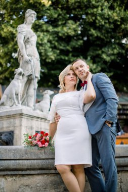 Olgun bir çift şehir çeşmesinin önünde sarılıyor, başka yere bakıyor ve hayal kuruyor.