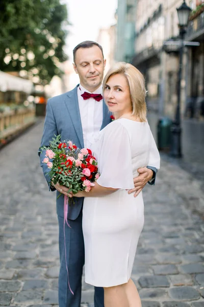 Felice coppia caucasica di mezza età, in posa con mazzo di fiori fuori nella bella strada della città vecchia — Foto Stock