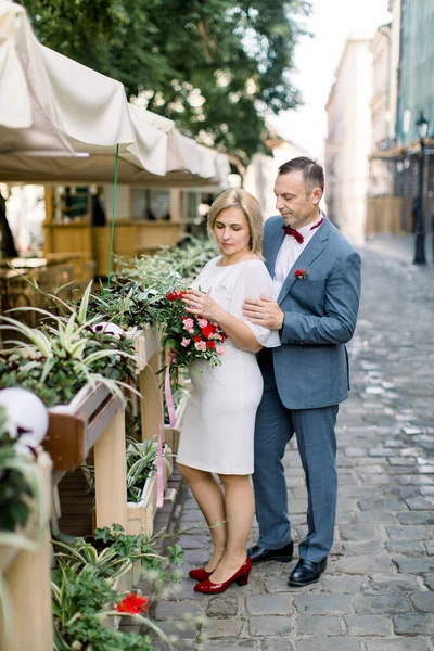 Mature couple in fashionable clothes, posing near flower pots decorations at outdoors city cafe — Stock Photo, Image