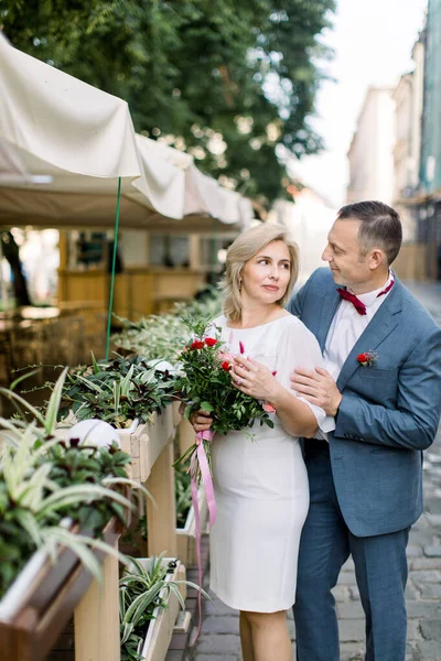 Volwassen paar in modieuze kleding, poseren in de buurt van bloempotten decoraties in de buitenlucht stad cafe — Stockfoto