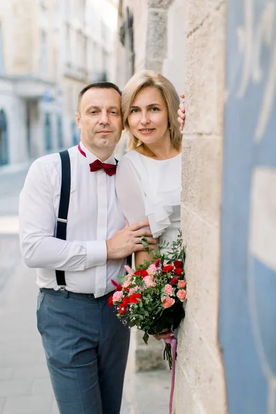 Šťastný romantický pár středního věku, pózování při pohledu na kameru v blízkosti staré historické budově města — Stock fotografie