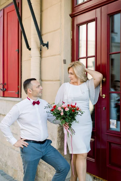 Šťastný dospělý milující pár, stojící venku ve městě, v blízkosti krásných starých červených dveří — Stock fotografie