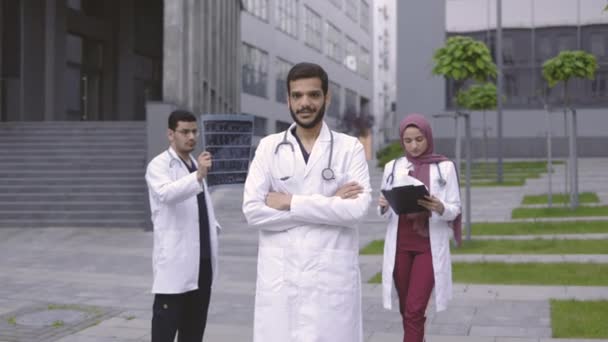 Squadra di tre medici arabi in piedi all'aperto vicino alla clinica moderna e al lavoro — Video Stock