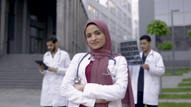 İki erkek arkadaşı dışarıda beklerken tesettürlü kadın Arap doktor gülümsüyor.