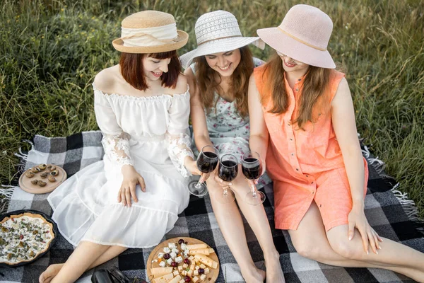 Vue d'angle supérieur de trois amies, assises sur la couverture de pique-nique et portant des verres à vin — Photo
