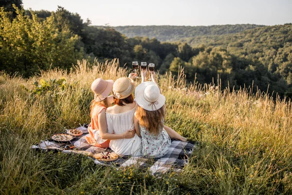 Visão traseira de três jovens amigas se divertindo, bebendo vinho tinto e curtindo piquenique de verão. — Fotografia de Stock