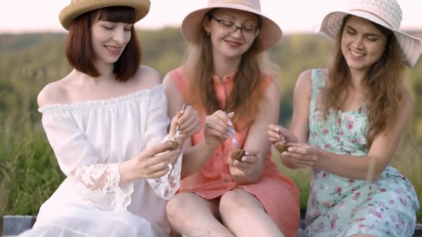 Tres hermosas amigas, disfrutan de un picnic, mostrando deliciosa comida, sabrosas escargotas asadas — Vídeo de stock