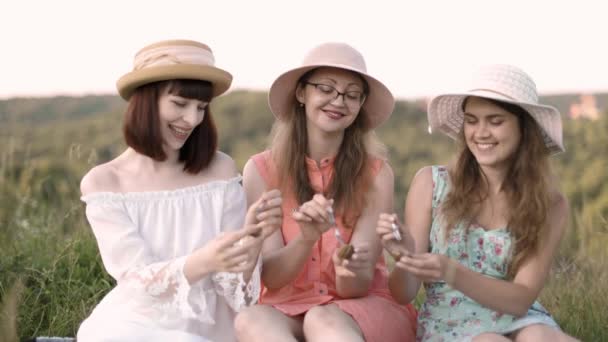 Τρεις όμορφες γυναίκες τρώνε νόστιμα σαλιγκάρια, κάθονται στο γρασίδι και κάνουν πικ-νικ πάρτι — Αρχείο Βίντεο