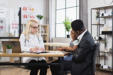 Bayan çocuk doktoru, çocuğunun muayenesi sırasında not alıyor. Babasıyla kliniğe gidiyor.