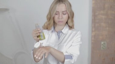 Sarışın, güzel bir kadın güzellik uzmanına yakın, elinde deri fırçasıyla bir şişe tutuyor. Tahıllı el soyma. Sağlıklı olmak ve ellerini ovuşturmak. Doktor kozmetik uzmanı kadın kozmetik ürünlerine el masajı yapıyor.