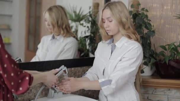 Porträtt av läkare kosmetolog, vacker ung kvinna med långt blont hår, bär vit medicinsk uniform tvätta och skölja av händerna i diskhon med hjälp av hennes assistent. — Stockvideo