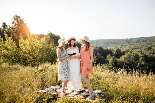 Trois belles femmes cliquetis verres de vin rouge, tout en se tenant sur l'herbe ayant temps de pique-nique confortable — Photo