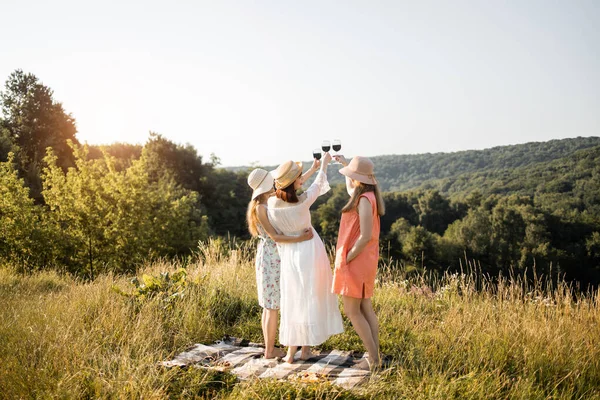 Vue arrière de trois jeunes amies qui s'amusent, boivent du vin rouge et profitent du pique-nique d'été. — Photo