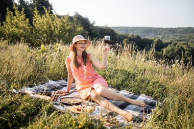 Dışarıdaki battaniyenin üzerinde kırmızı şarap bardağıyla oturan hoş bayan.