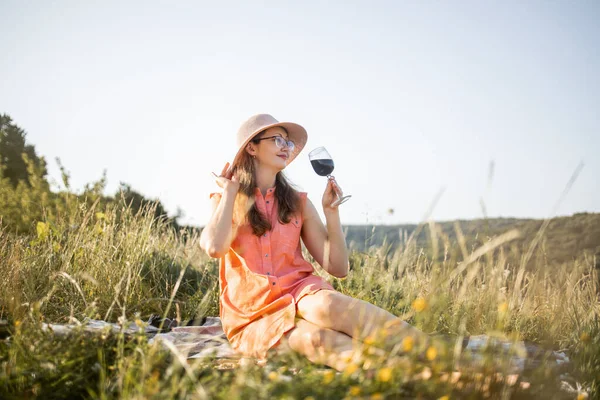 밖에 담요 위에 앉아 있는 붉은 포도주 한 잔을 들고 있는 매혹적 인 여인 — 스톡 사진