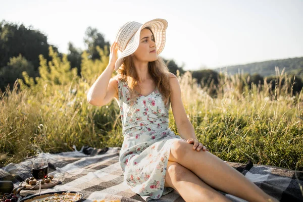 Junge Frau schaut weg, sitzt auf Plaid mit leckerem Essen und Früchten und genießt den Sommertag. — Stockfoto