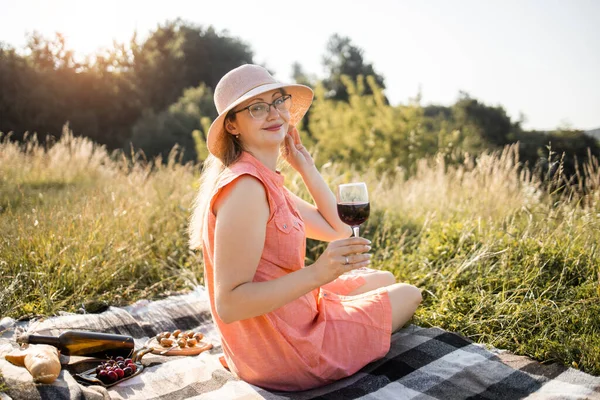 멋진 옷을 입고 모자를 쓰고 자연 피크닉에 앉아 빨간 포도주를 마시는 여성 — 스톡 사진