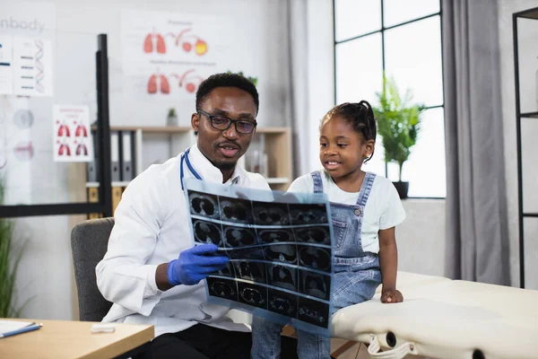 Médico pediatra do sexo masculino, mostrando resultados de tomografia computadorizada de raios-x para menina pequena criança africana — Fotografia de Stock