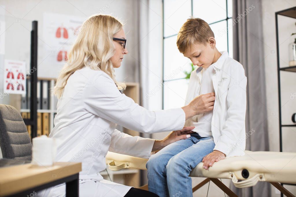 Doctor using stethoscope for listening boys lungs at clinic