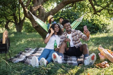 Doğada piknik yaparken akıllı telefon kullanan dört arkadaş.