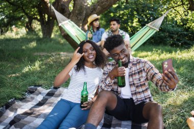 Mutlu çeşitli arkadaşlar piknik yapıyor ve cep telefonu kullanıyor.