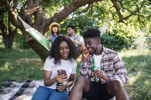 Amis multiraciaux utilisant mobile et boire de la bière en plein air — Photo