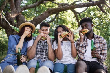 Çeşitli arkadaşlar bira içip dışarıda hamburger yiyorlar.