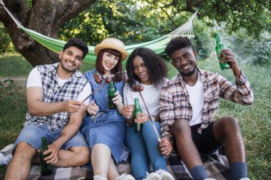 Mutlu arkadaşlar doğada bira içip sosis yiyorlar.