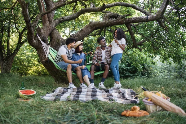 Τέσσερις πολυπολιτισμικοί φίλοι κάνουν πικ-νικ στον καλοκαιρινό κήπο — Φωτογραφία Αρχείου