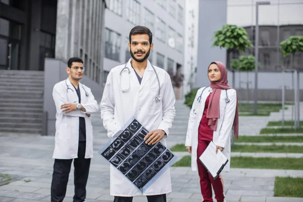 Squadra di tre medici arabi in piedi all'aperto vicino alla clinica moderna e al lavoro — Foto Stock