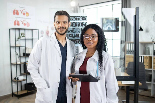 Medici multietnici in uffici moderni al chiuso. Parete di vetro con radiografia e tomografia dietro — Foto Stock