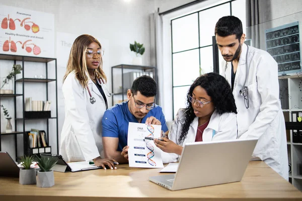 Четыре разнородных врача генетики, имеющие онлайн встречу с коллегой на ноутбуке — стоковое фото