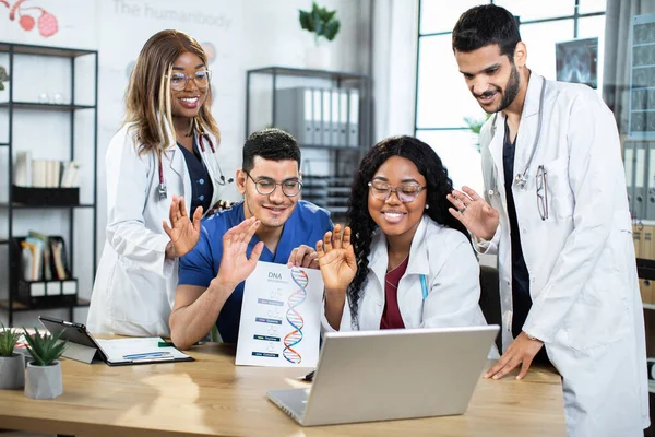 Çok ırklı genetik doktorları. Üniformalı bilim adamları video görüşmeleri sırasında meslektaşlarına el sallıyorlar. — Stok fotoğraf