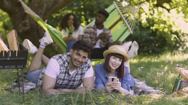 Cuatro amigos multirraciales relajándose, charlando y bebiendo en el picnic al aire libre — Vídeos de Stock