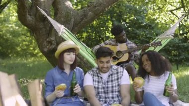 Arkadaşlar yiyip içerken siyah adam gitar çalıyor.