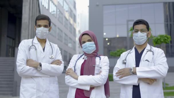 Tres trabajadores sanitarios multiétnicos con máscaras faciales, posando con los brazos cruzados al aire libre — Vídeos de Stock