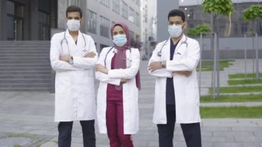 Maskeli üç doktordan oluşan bir ekip modern kliniğin önünde baş parmak gösteriyor.