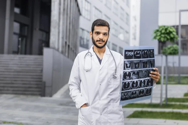 Maschio medico indiano arabo, tenendo i pazienti tomografia scansione, in posa vicino ospedale moderno — Foto Stock