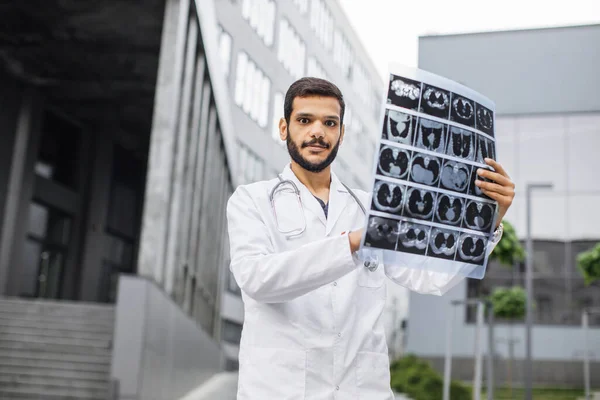 Maschio medico indiano arabo, tenendo i pazienti tomografia scansione, in posa vicino ospedale moderno — Foto Stock