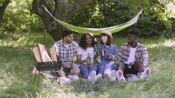 Cuatro amigos multirraciales haciendo picnic en el jardín — Vídeo de stock