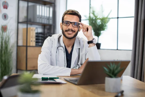Maschio medico malese in occhiali da vista, seduto a tavola con computer portatile pc in ufficio moderno — Foto Stock