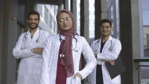 Медицинская команда с молодой очаровательной леди в хиджабе, ведущей, позирующей за пределами больницы — стоковое видео
