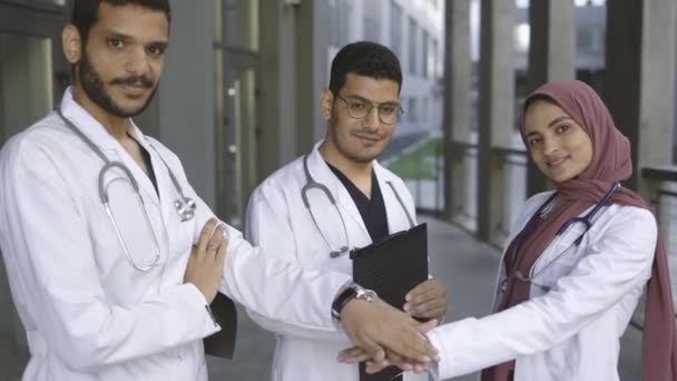 Zwei gut aussehende Ärzte und ihre hübsche Kollegin im Hijab, die Hände stapelnd — Stockvideo