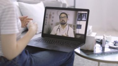 Bilgisayarda erkek doktor görüntüsü, kadın hastayla çevrimiçi video görüşmesi.