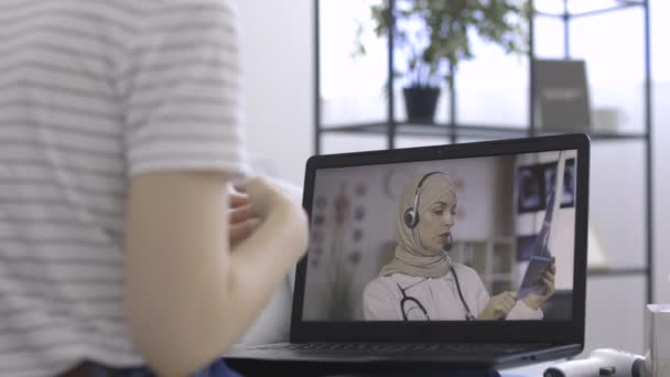 Patiente ayant un chat vidéo avec une femme arabe médecin sur ordinateur portable PC à la maison — Video