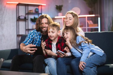 Mutlu aile koltukta otururken cep telefonuyla selfie çekiyor.