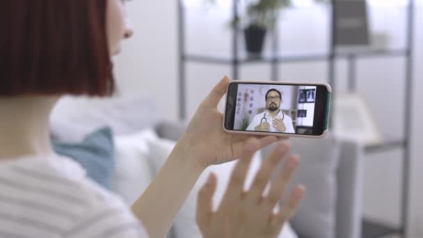 Przez ramię widok ekranu telefonu z mężczyzna kaukaski lekarz rozmawiający z pacjentką — Wideo stockowe