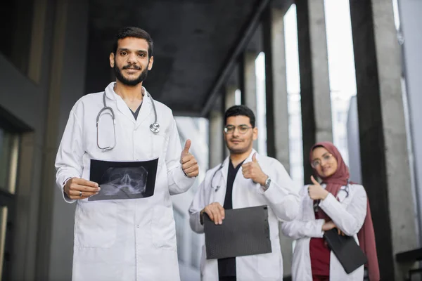 白い研究室のコートのアラブ医療チームは、列に折り畳まれた腕で立って親指を表示 — ストック写真