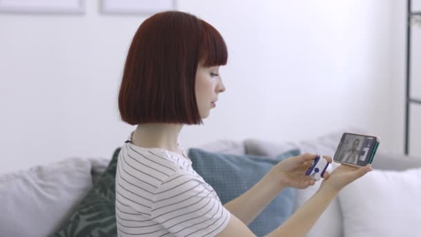 Femme assise sur le canapé à la maison avec oxymètre de pouls, parler avec un médecin masculin en ligne à l'aide d'un smartphone — Video